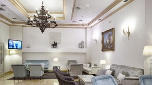 Un salón amplio con una araña, diversas opciones de asientos, un televisor de pantalla plana y decoración mural.