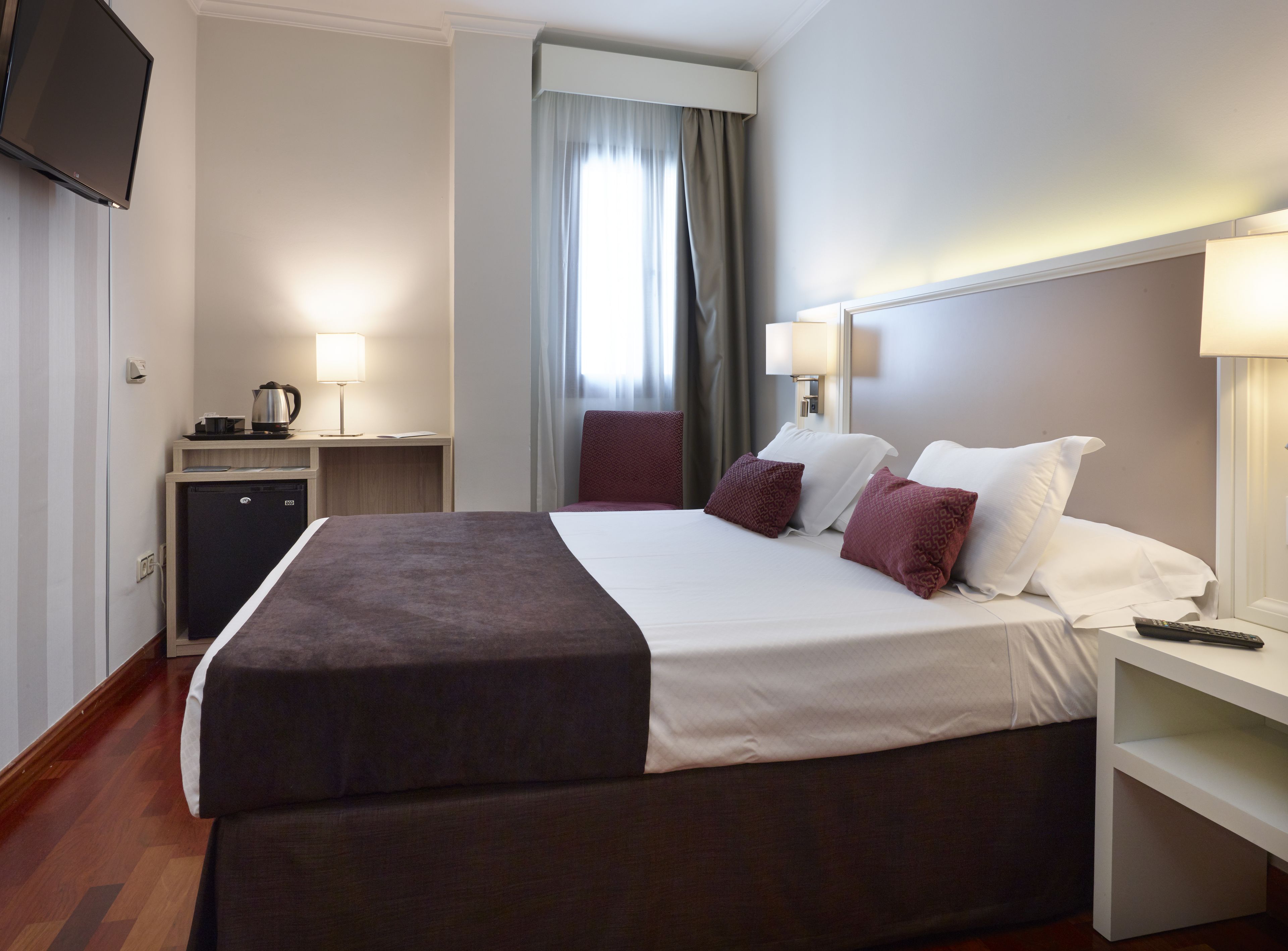 Une chambre d’hôtel équipée d’un lit, de tables de chevet, d’une télévision, d’un mini-réfrigérateur et d’une fenêtre avec des rideaux.