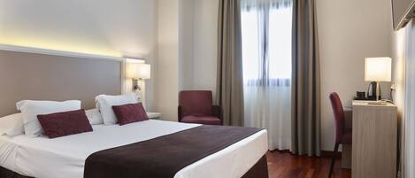 A hotel room with a large bed, two bedside tables, a desk, and a chair.