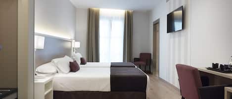 Une chambre d’hôtel avec deux lits, un bureau, une chaise, une télévision et une fenêtre avec des rideaux.