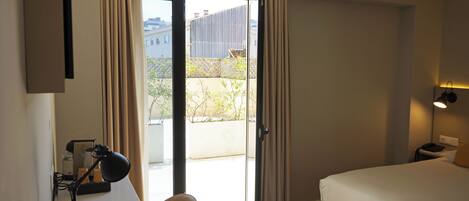 Habitación de hotel con cama, escritorio, silla y vista a un espacio exterior por una puerta corrediza de vidrio.