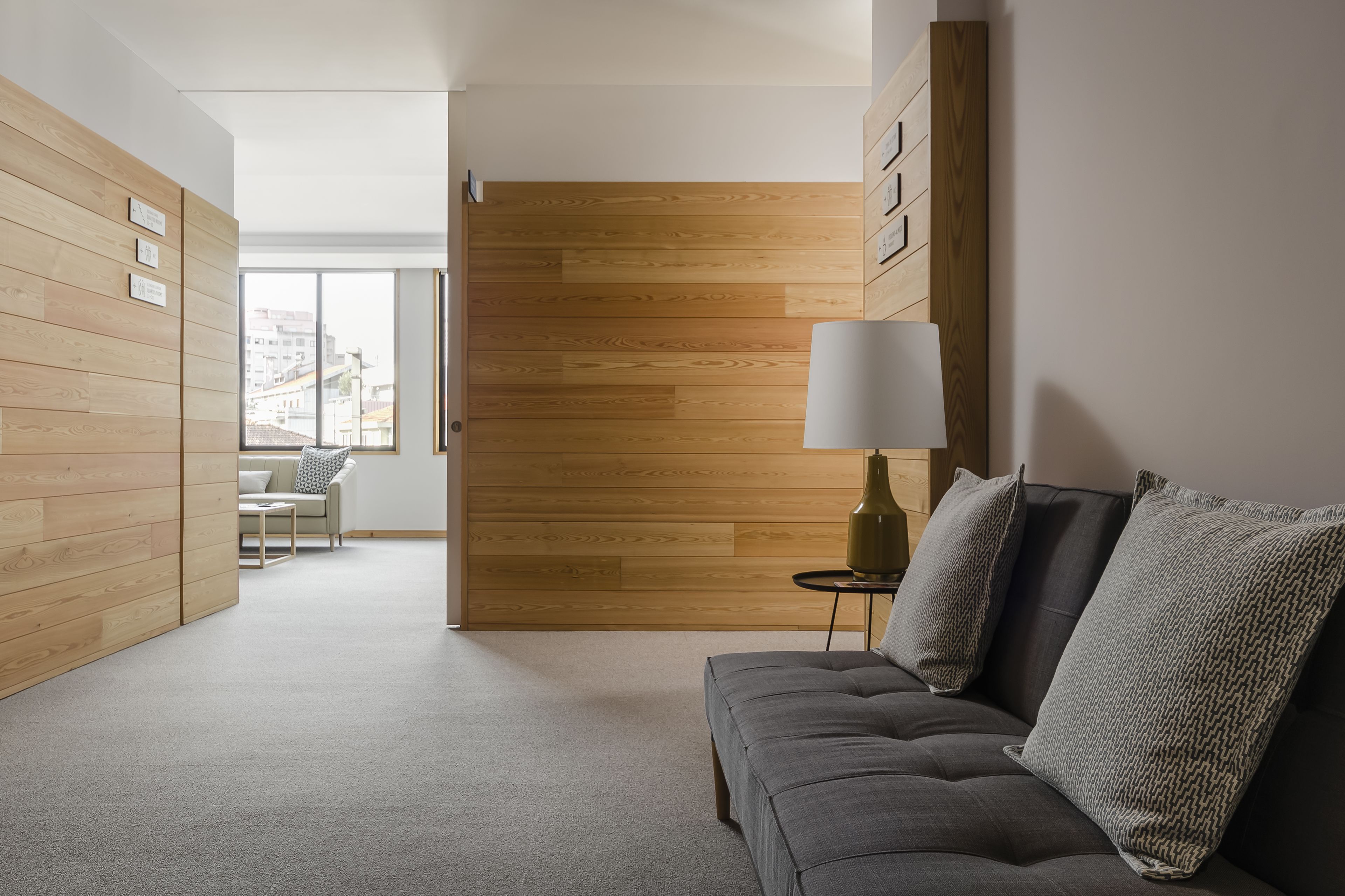 Una sala moderna con un sofá gris, una lámpara y un revestimiento de pared de madera.