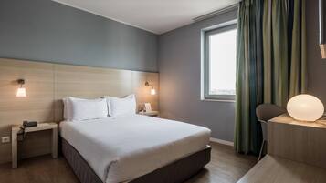 Una habitación de hotel moderna con una cama grande, lámparas de noche, un escritorio con lámpara y vistas a la ciudad a través de una ventana.