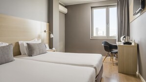 Habitación de hotel con dos camas, un escritorio, una silla, un televisor y una ventana con cortinas.