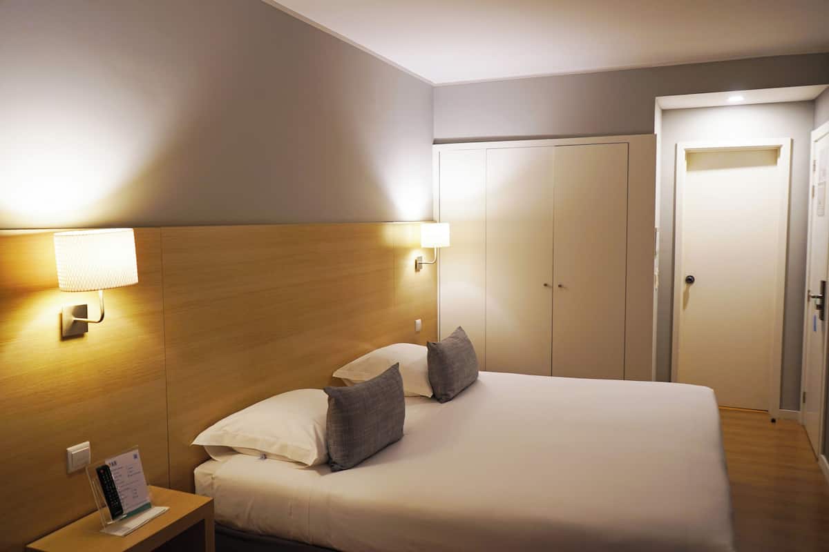 A hotel room with a bed, nightstand, and a wardrobe.