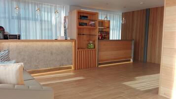 Eine moderne Hotelhalle mit einem Holzbuchungsschalter, einer Couch und einem großen Fenster mit transparenten Vorhängen.