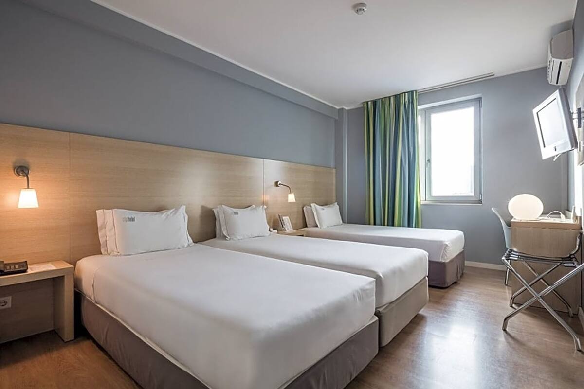 A hotel room with two beds, a desk, a chair, a TV, and a window with curtains.
