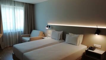 Habitación de hotel con dos camas, una silla, un escritorio y una mesita de noche con un teléfono.
