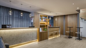 Una moderna zona de recepción con mostrador de madera, taburetes tipo bar e iluminación colgante.