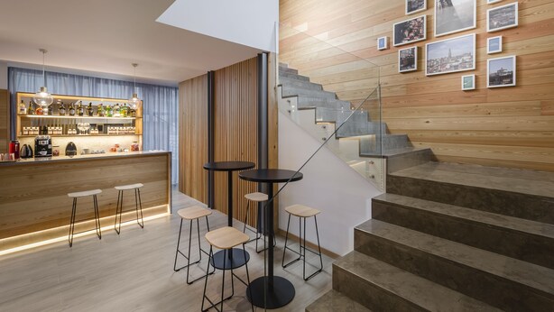 Un bar moderno con taburetes, una barra y una escalera de madera decorada con cuadros.