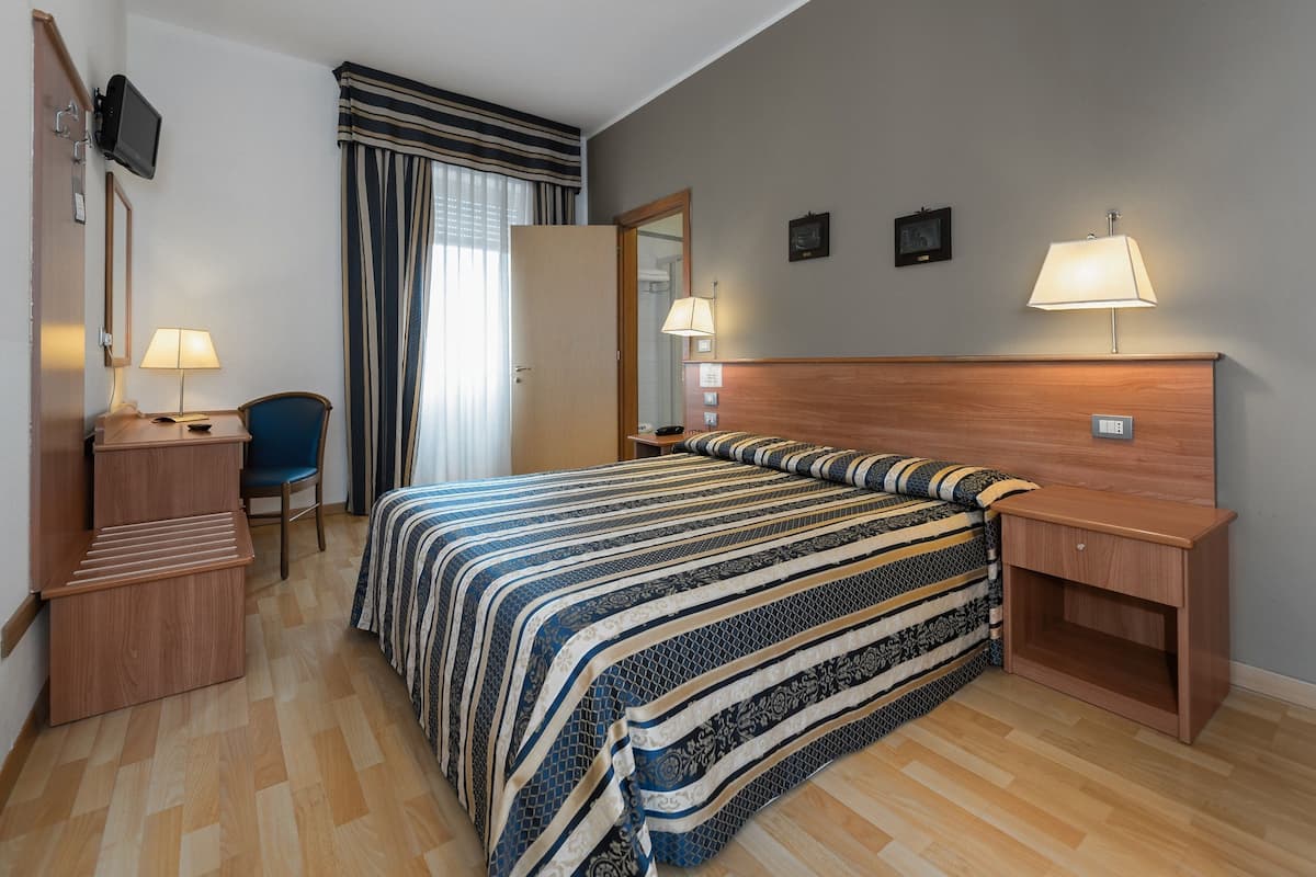 A hotel room with a bed, a desk, a chair, a TV, and a nightstand.