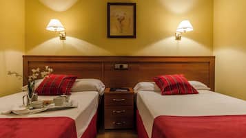 Habitación de hotel con dos camas, cada una con almohada roja y ropa de cama blanca. Hay mesitas de noche con lámparas, una obra de arte enmarcada en la pared y una bandeja con alimentos para el desayuno sobre la cama de la izquierda.