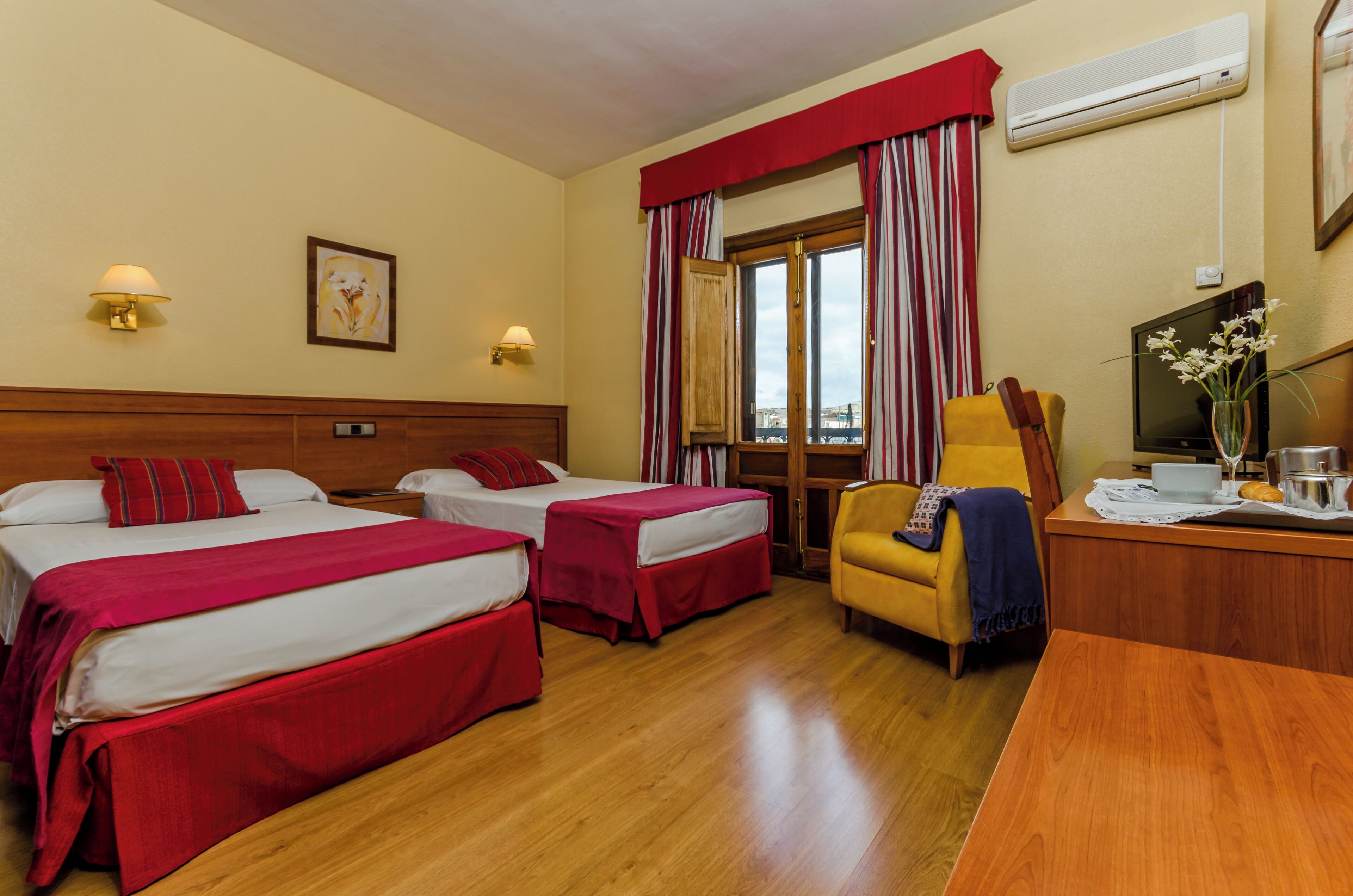 A hotel room with two beds, a desk, a chair, a TV, and a window with curtains.