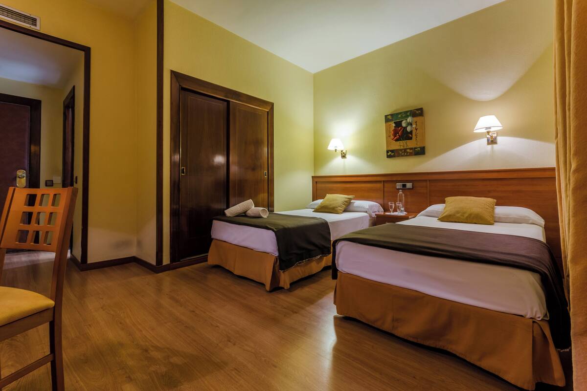 Habitación de hotel con dos camas, piso de madera, un armario de madera, una silla y un cuadro en la pared.