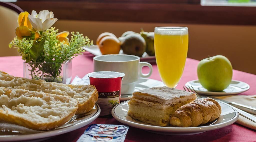 A breakfast setting with bread, pastries, a fruit bowl, a glass of orange juice, and a cup of coffee on a table.