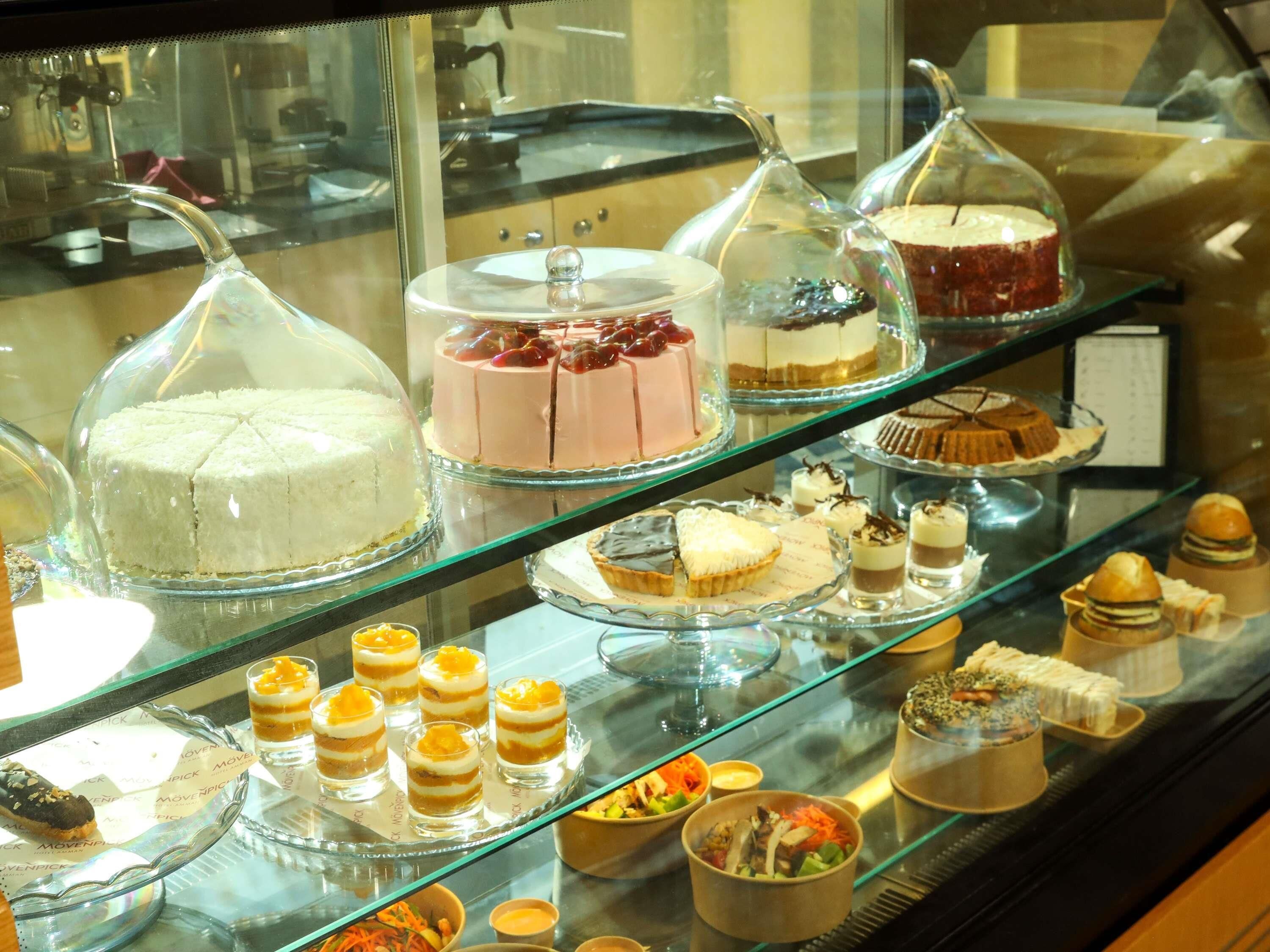 Diverse desserts uitgestald in een glazen vitrine, waaronder taarten, gebakjes en kleine desserts.