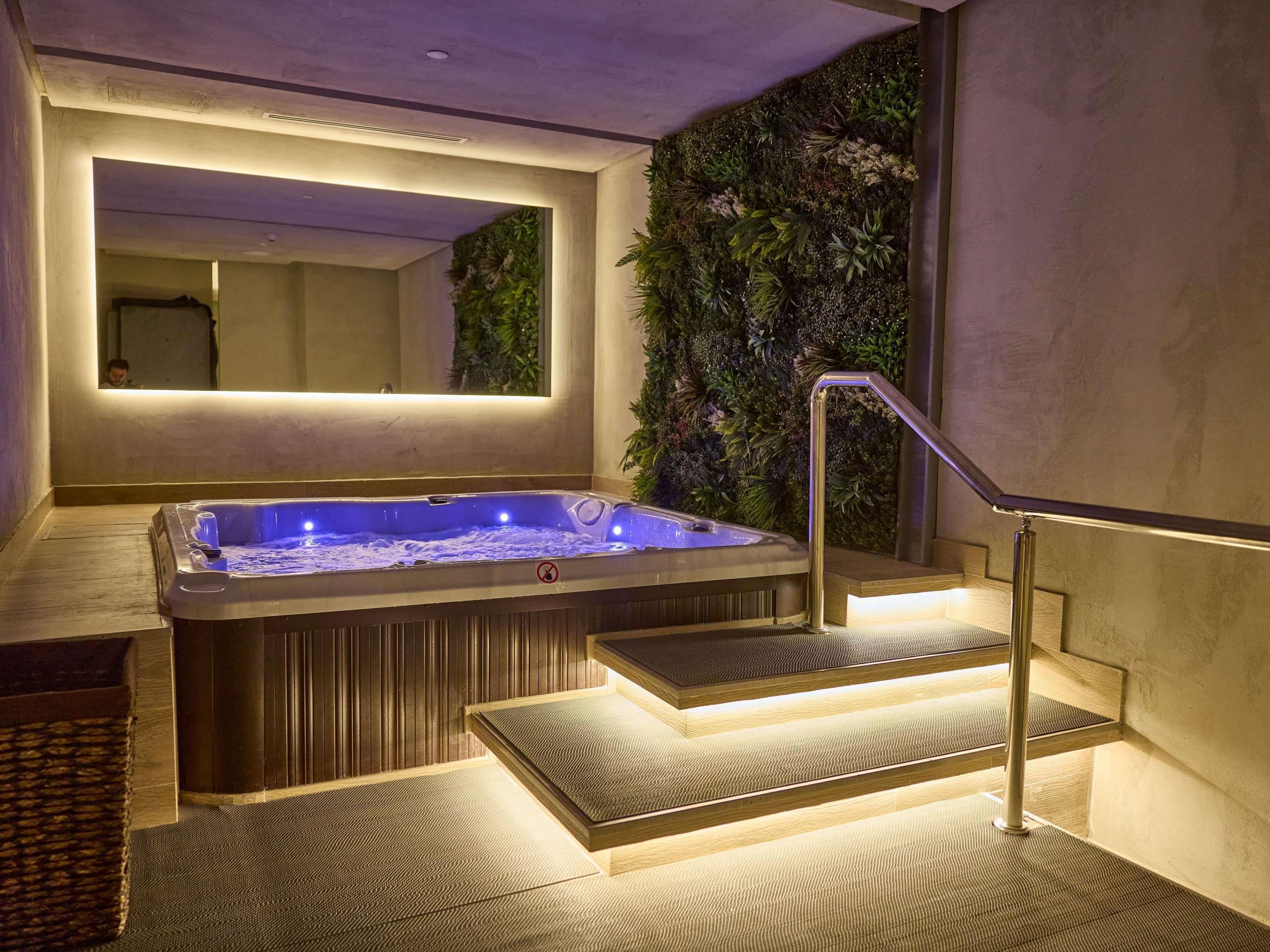 A hot tub with steps leading up to it, a wall-mounted mirror, and a textured floor.