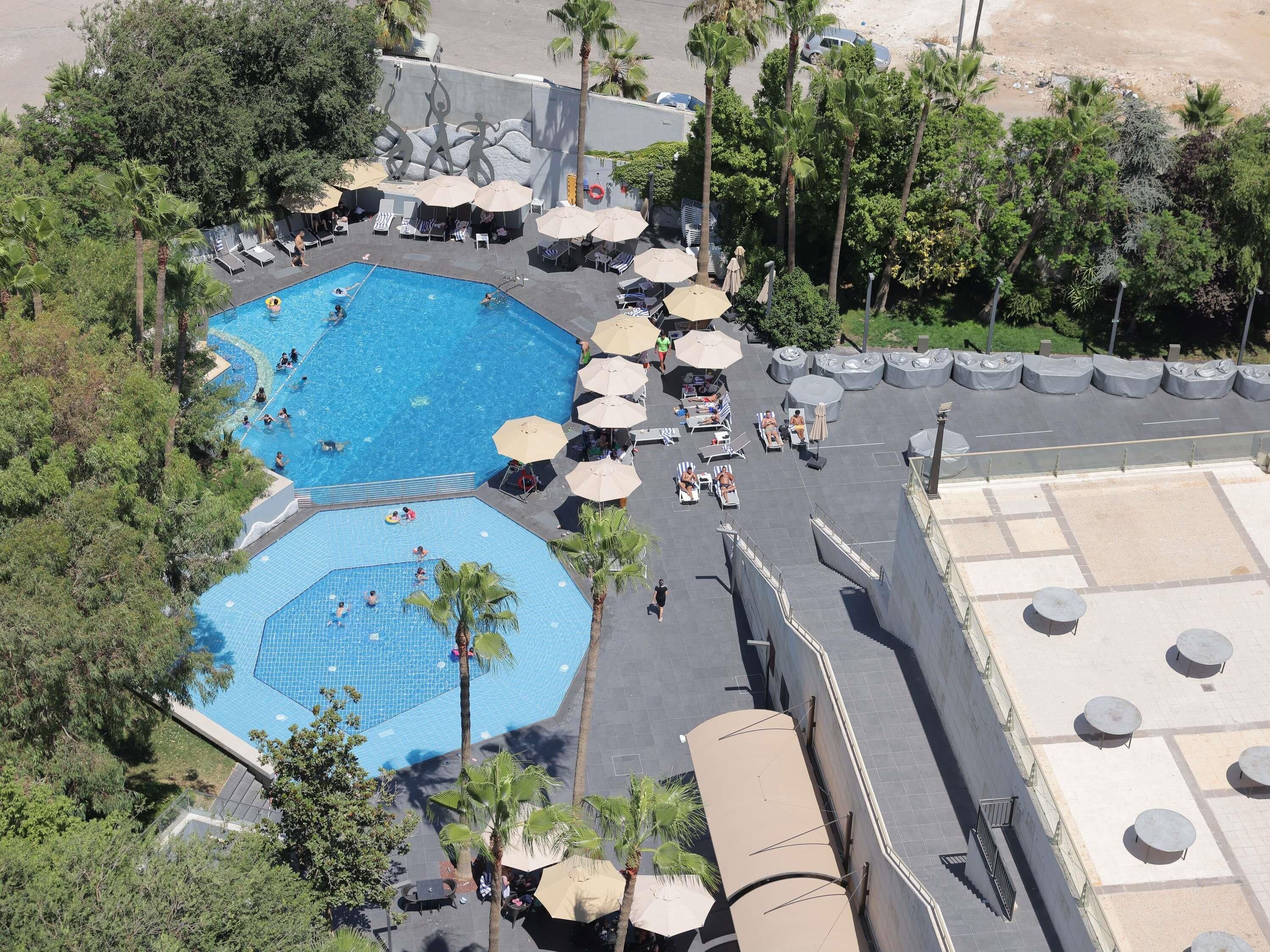 A rooftop pool area with multiple swimming pools, sun loungers, and umbrellas.