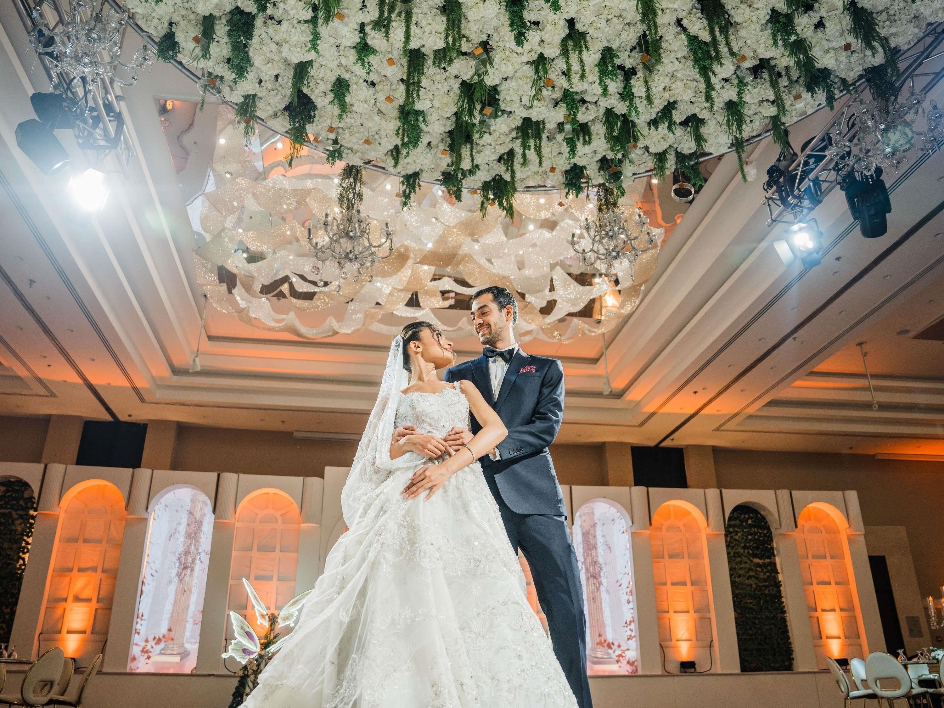 A couple embracing in a decorated indoor setting with chandeliers and floral arrangements.