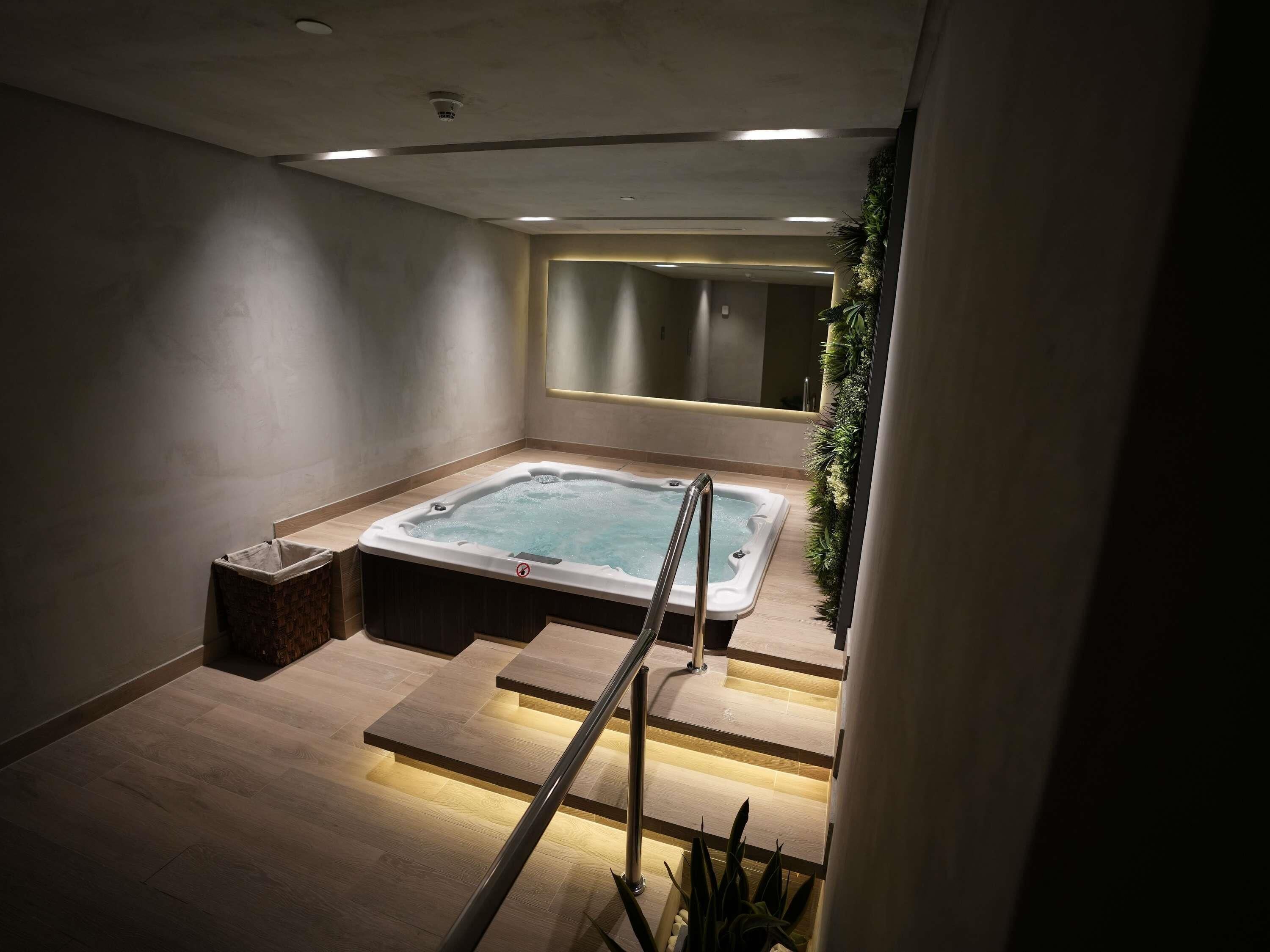 Un baño moderno con bañera de hidromasaje, suelo de madera, espejo y una escalera.