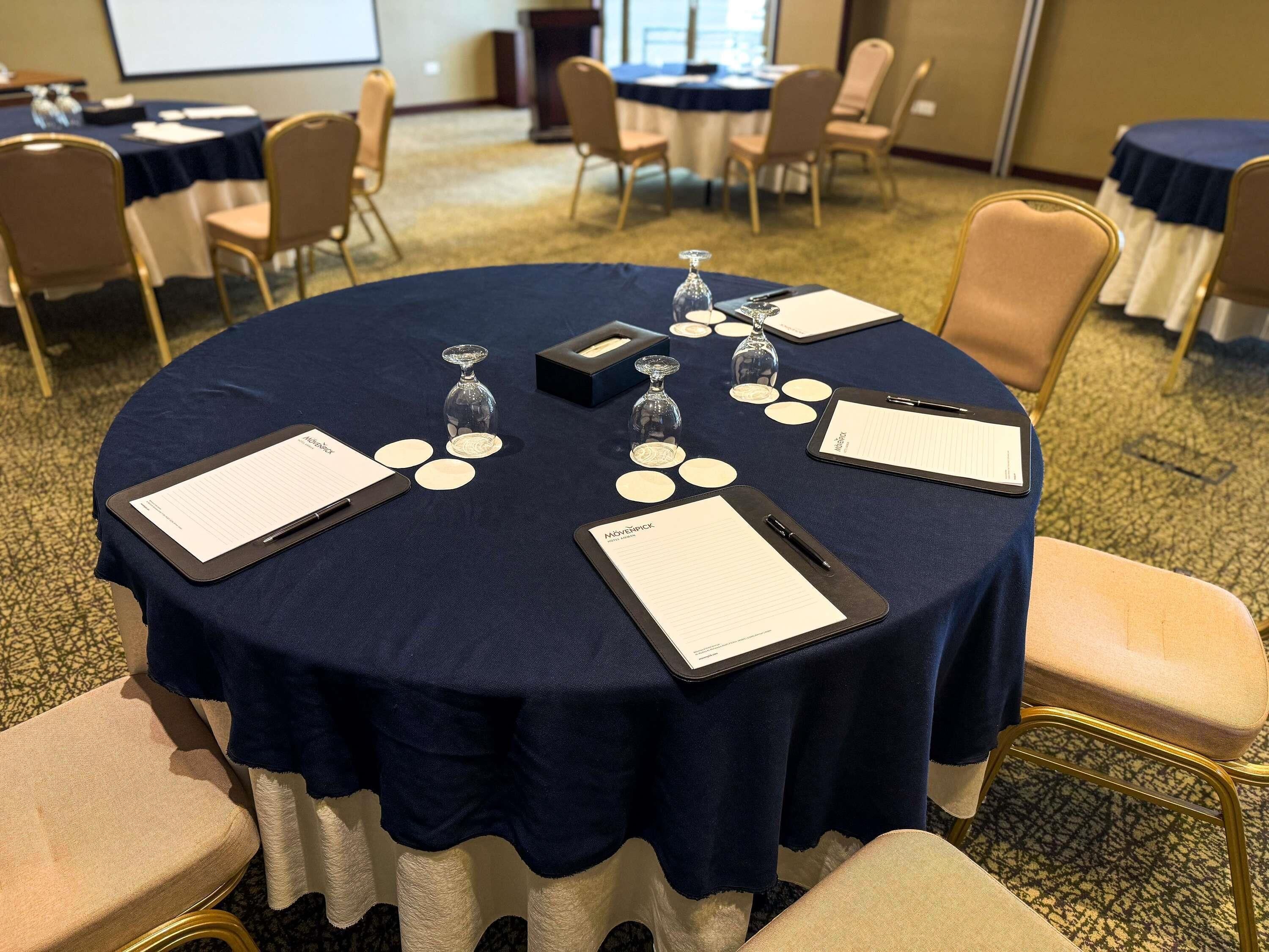 A conference room with a round table, chairs, nameplates, and a projector screen.