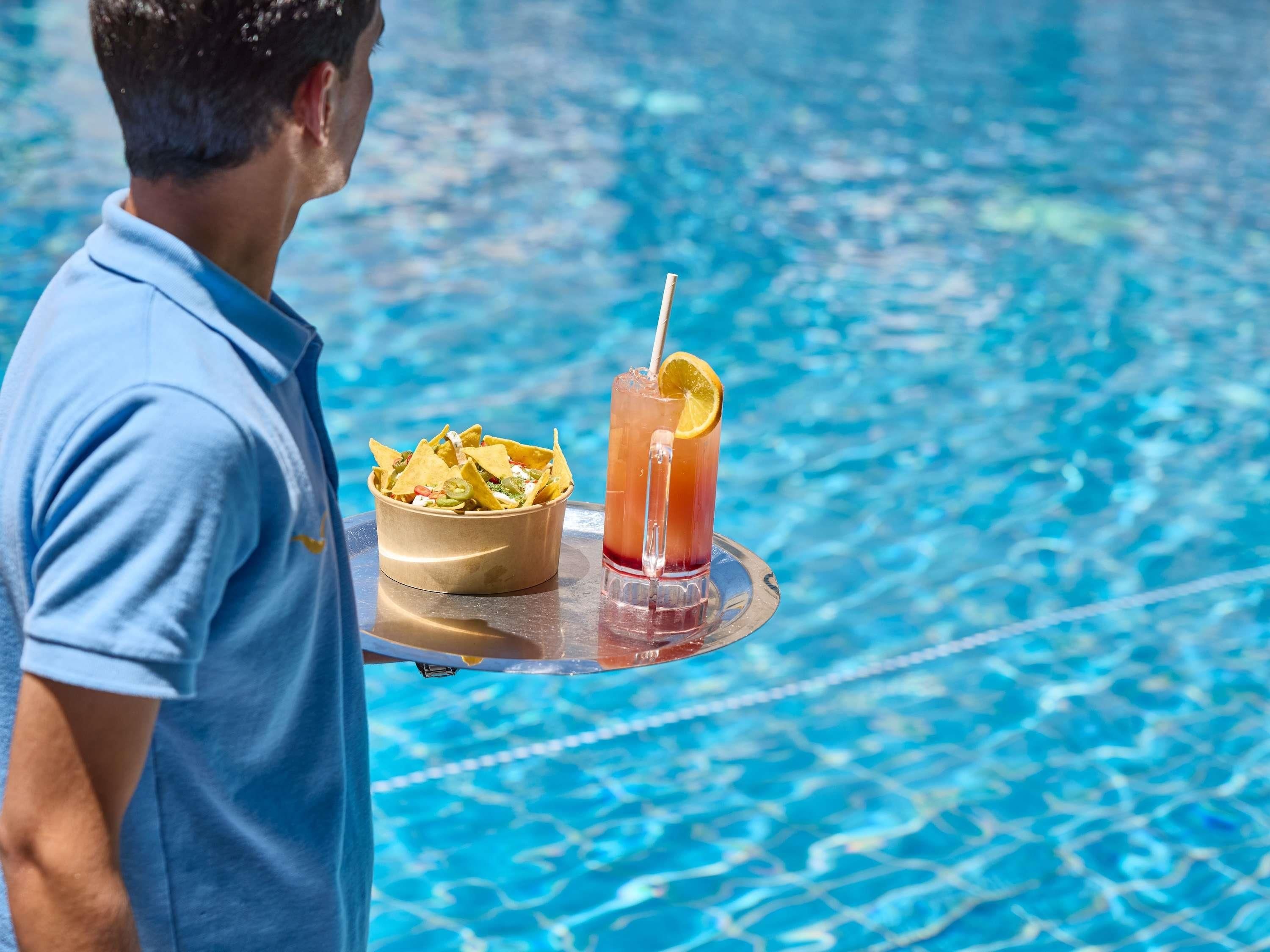 A person holding a tray with nachos and a drink near a pool.