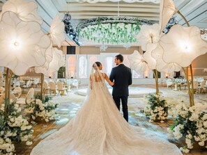 Una cerimonia nuziale con sposa e sposo in una sala decorata, con composizioni floreali e lampadari.