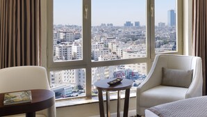 Habitación de hotel con un ventanal grande que ofrece vistas a la ciudad, un sofá, una mesita y un control remoto sobre la mesa.