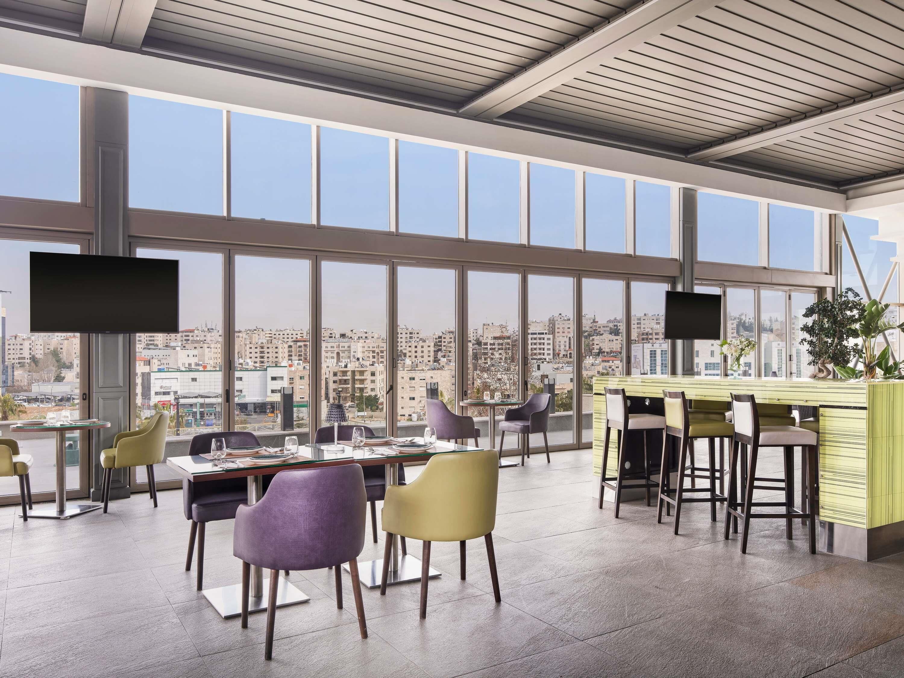 Een modern restaurant met grote ramen met uitzicht over de stad, meerdere zithoeken en een bar.
