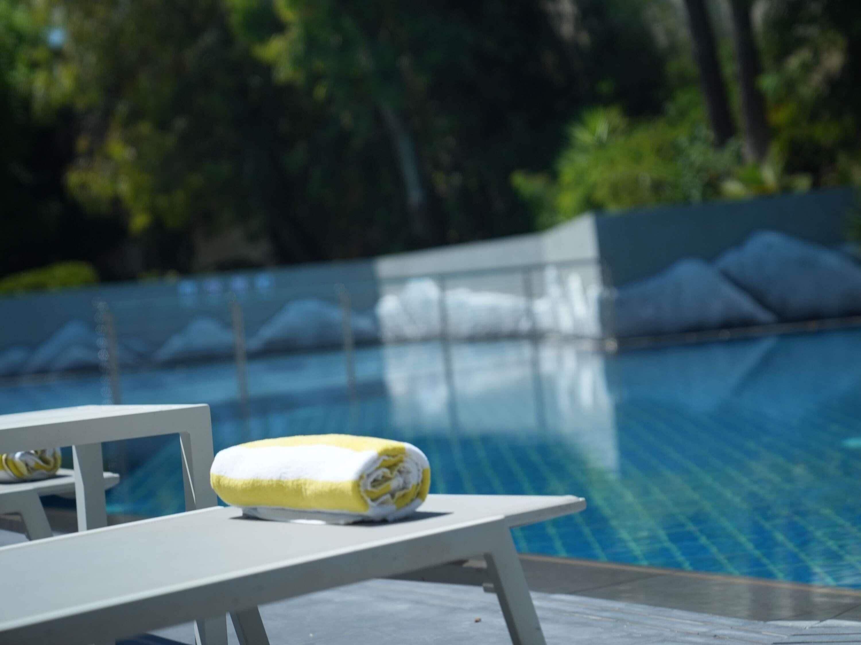 Zona de piscina con una silla de descanso y una toalla enrollada.