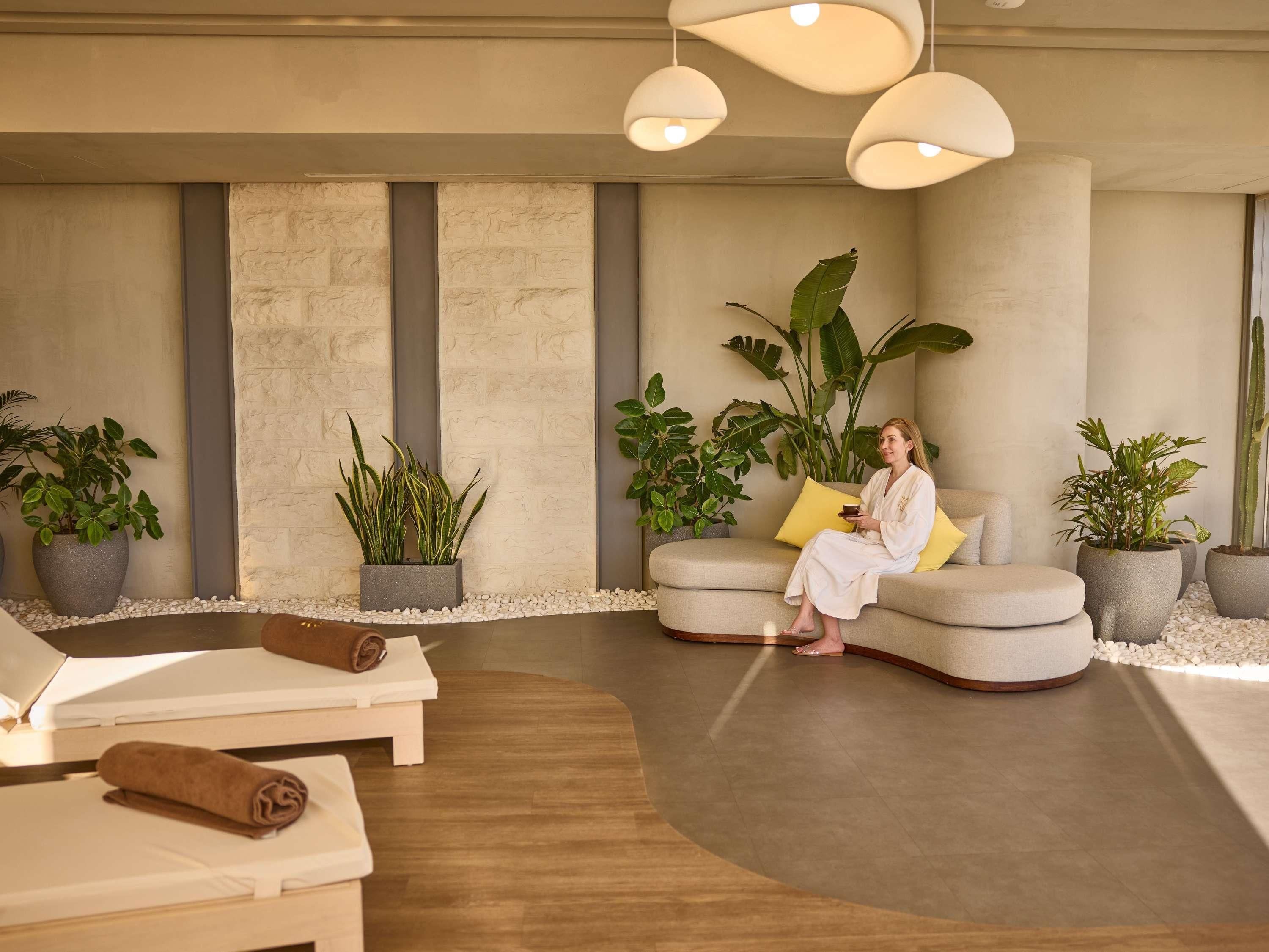 Un espacio de spa con zona de estar, plantas y una persona relajándose.