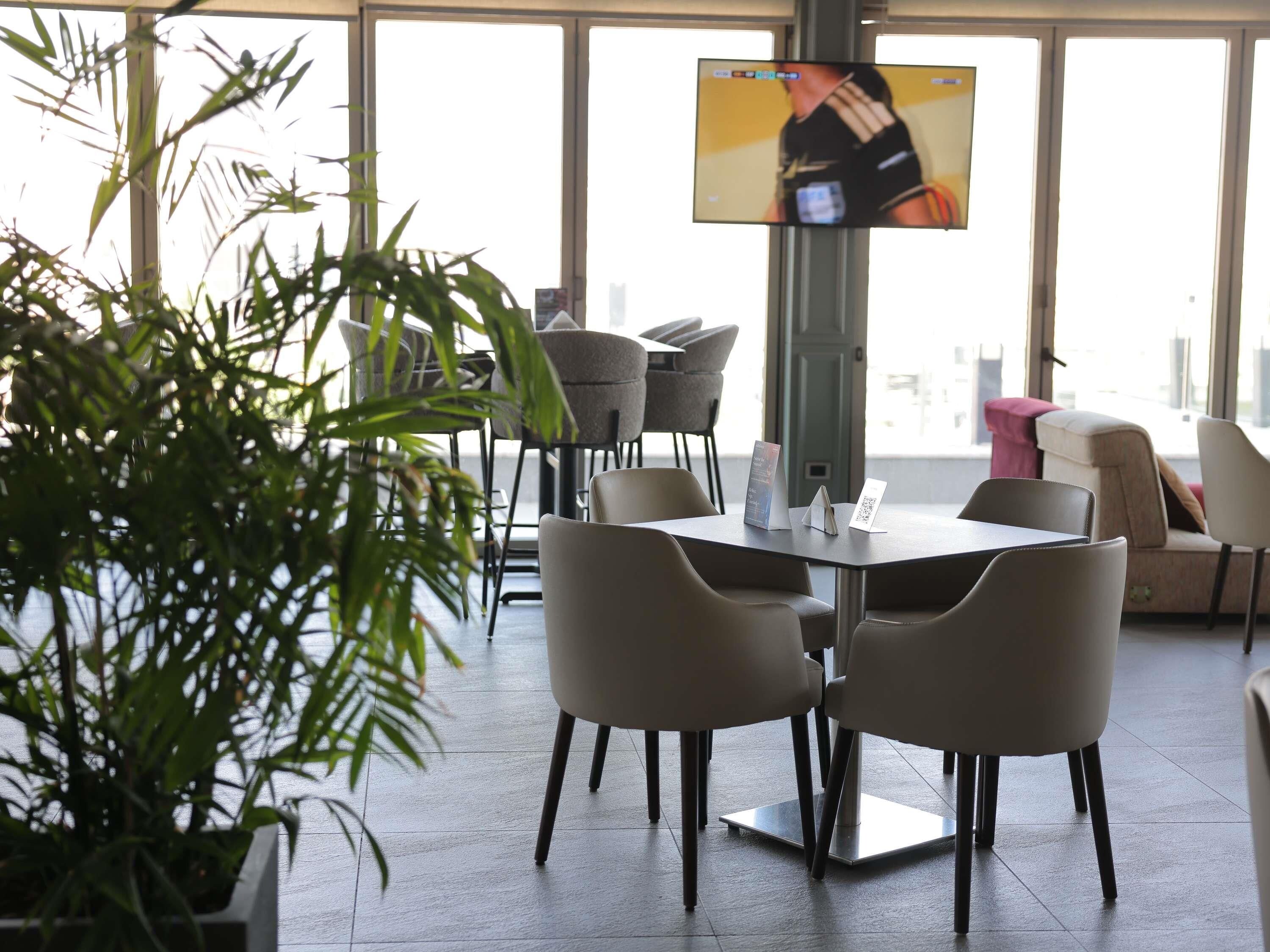 Un espacio interior moderno con una mesa y sillas, un televisor en la pared y una planta grande en maceta.