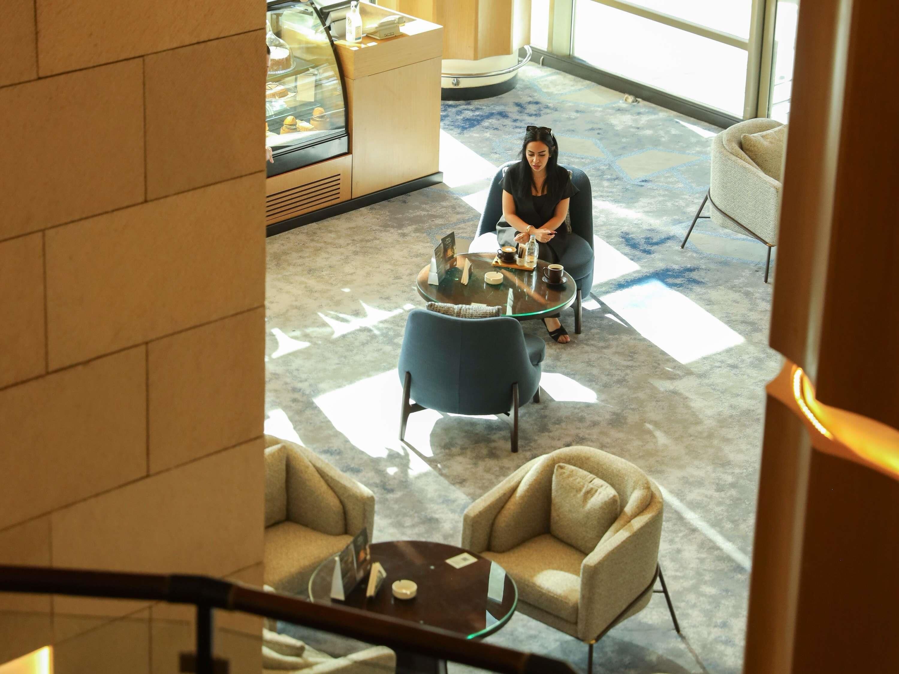 A woman sitting at a glass table with a coffee cup, a smartphone, and a menu.
