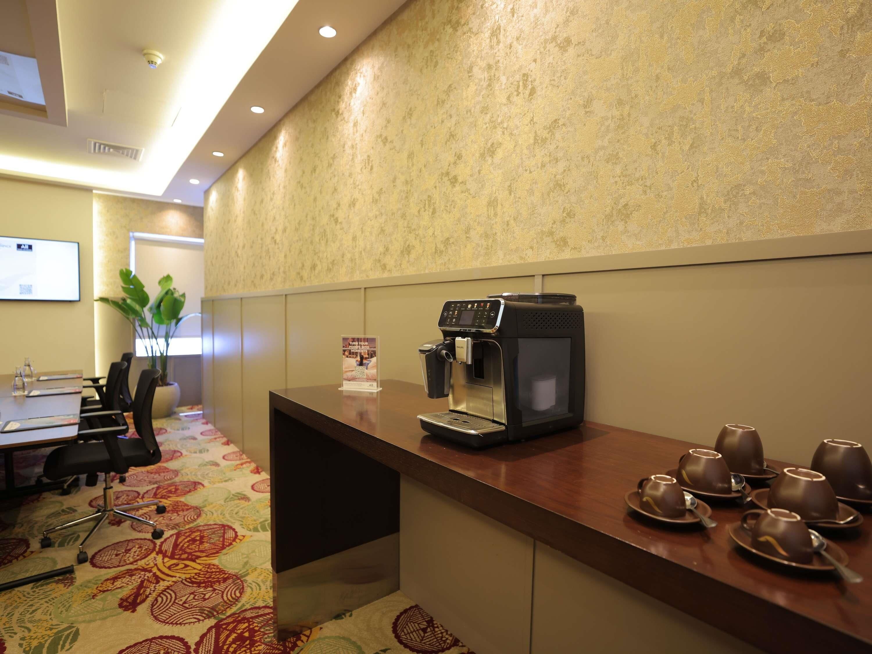 A conference room with a coffee machine, chairs, a table, and a plant.