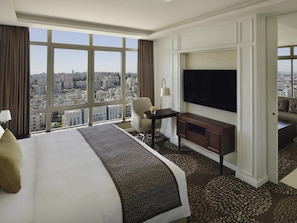 A hotel room with a large bed, a TV, a desk, and a view of the city. - Mövenpick Hotel Amman (Amman)
