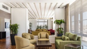 Una sala de estar moderna con suelo de madera, sofás beige y verdes, una mesa de centro y ventanas amplias con cortinas.