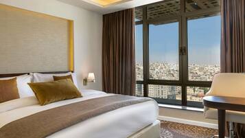 Habitación de hotel con una cama grande, un escritorio, una silla, una ventana con vistas a la ciudad y una lámpara de pared.