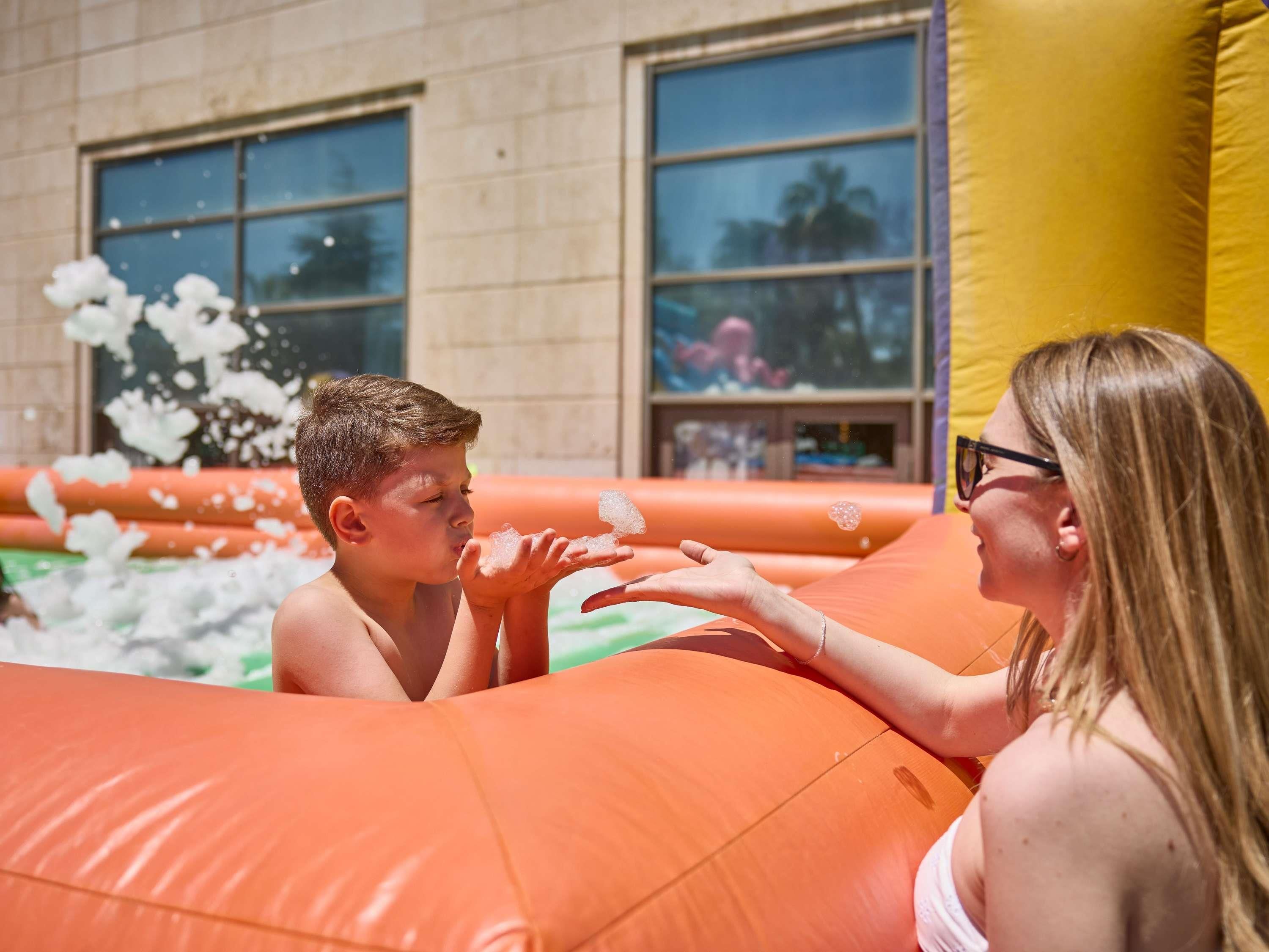 Una persona soplando burbujas hacia otra en un área de piscina inflable.