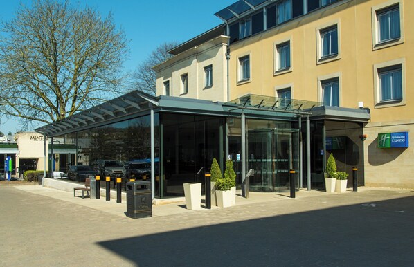 A modern hotel with a glass entrance, outdoor seating, and a Holiday Inn Express sign.
