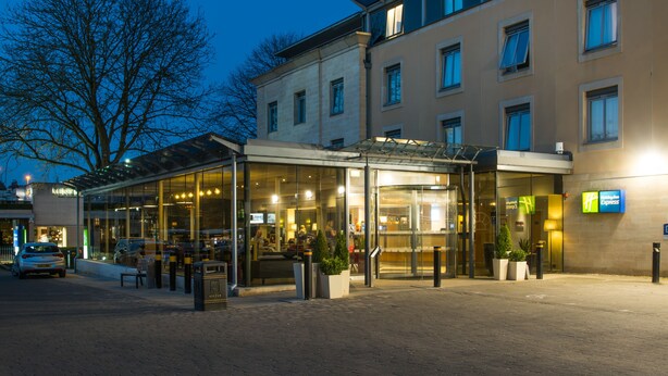 A hotel with a glass entrance, outdoor seating, and a visible sign for 'Express'.