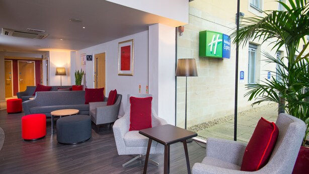A modern hotel lobby with grey sofas, red cushions, and a small wooden table. - Holiday Inn Express Bath by IHG (Bath)