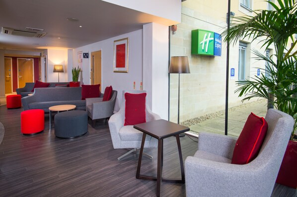 Un hall d’hôtel moderne avec des canapés gris, des coussins rouges et une petite table en bois.
