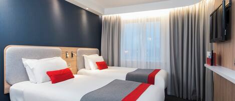A hotel room with two beds, a flat-screen TV, a window with curtains, and a wooden wall.
