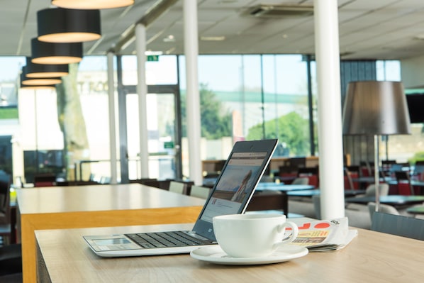 A laptop on a table with a white cup and saucer, and a newspaper. - Holiday Inn Express Bath by IHG (Bath)