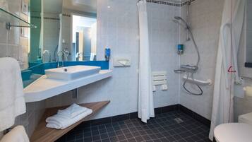 Un baño moderno con lavamanos, espejo, ducha y retrete.