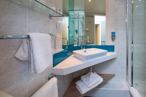 A modern bathroom with a glass shower enclosure, a white sink, and a wooden shelf.