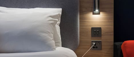 A neatly made bed with a white pillow and a headboard with a textured grey panel.