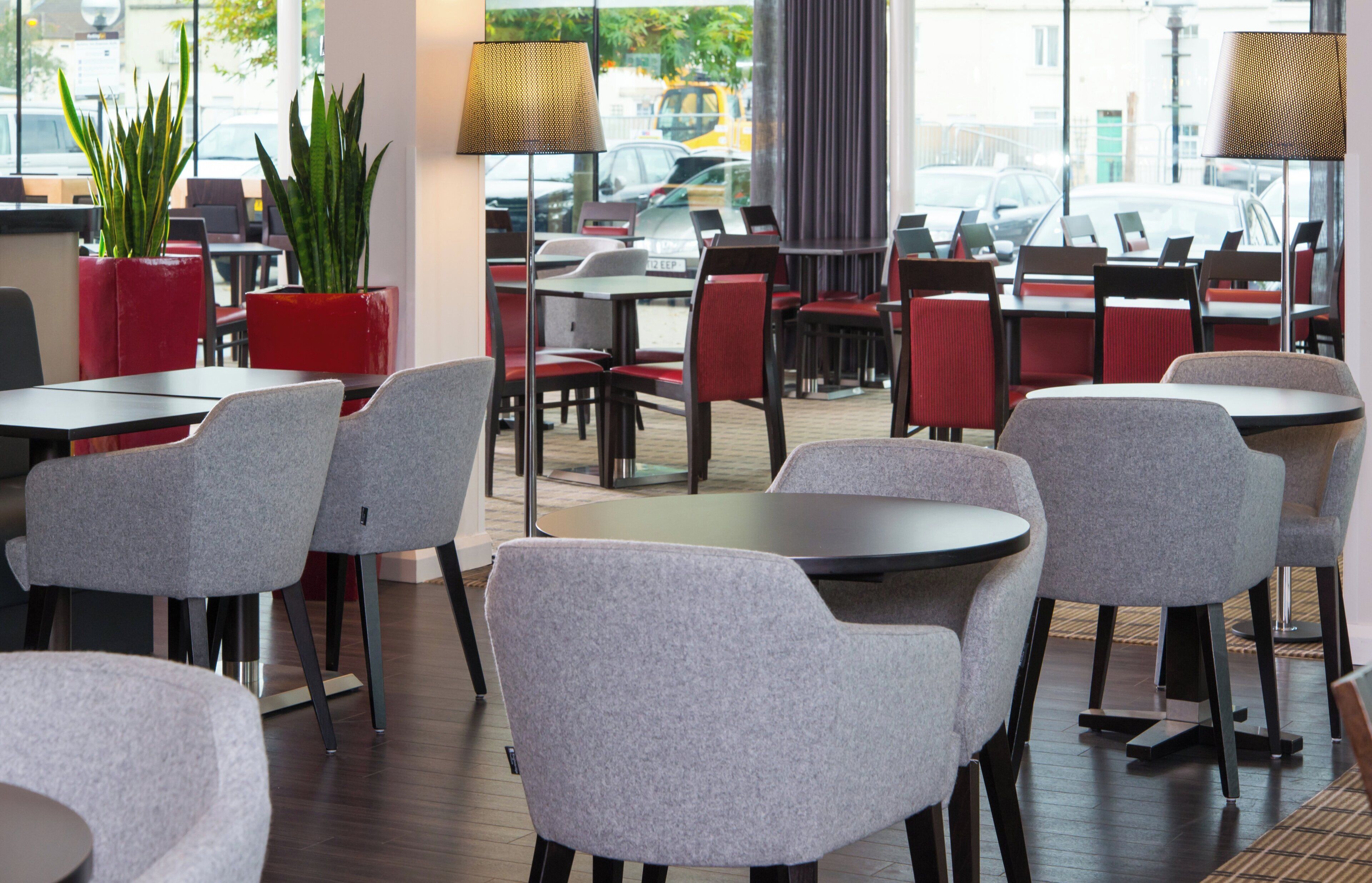 A modern indoor seating area with tables and chairs, large windows, and potted plants.