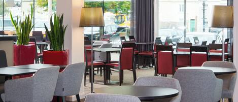 A modern indoor seating area with tables and chairs, large windows, and potted plants.