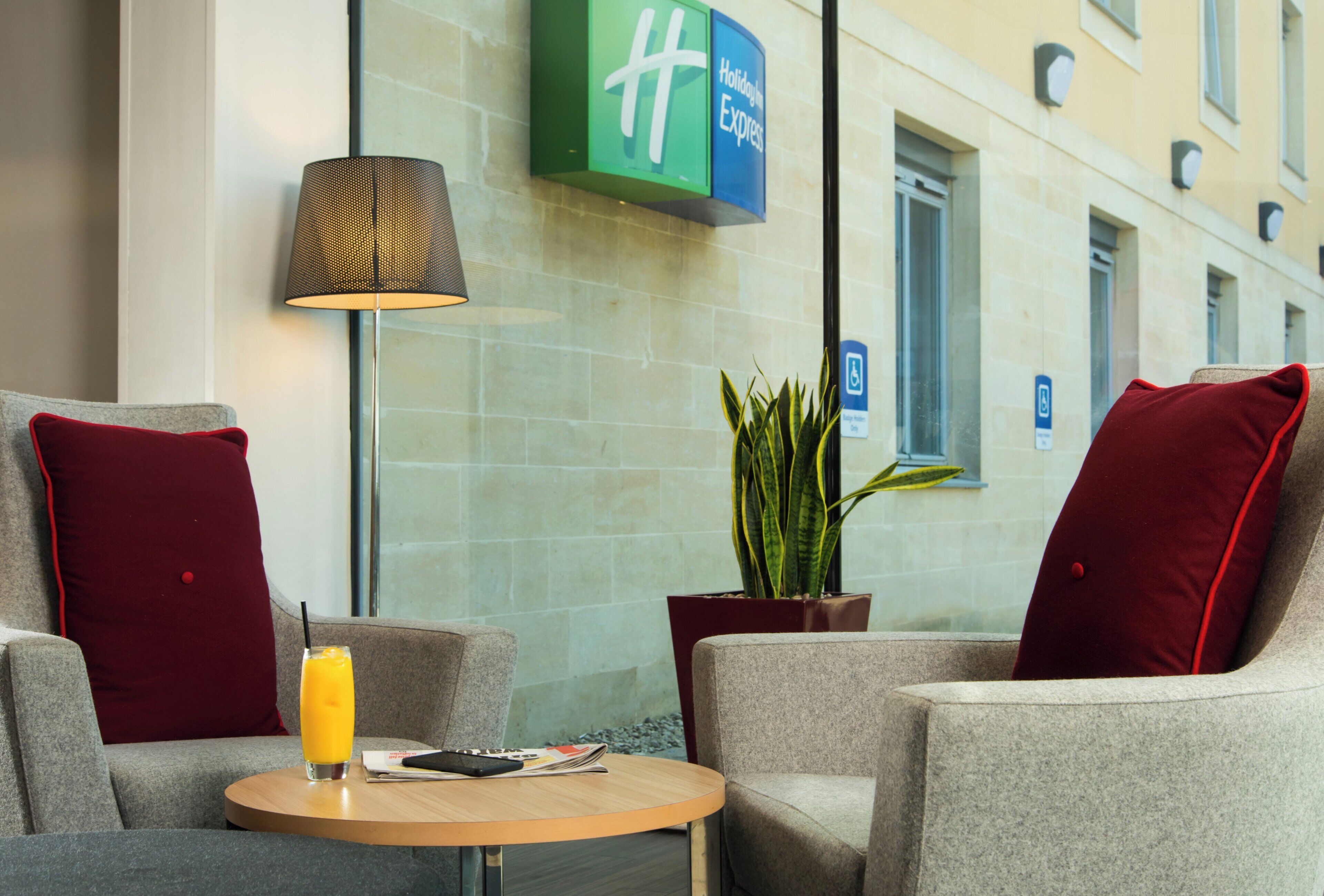 Een hotel lobby met een zithoek, met twee fauteuils, een tafel met een drankje en een menukaart, een lamp en een plant.